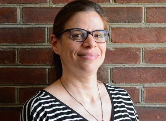 Headshot of Dr. Ariel Bierbaum standing in front of a red brick wall.